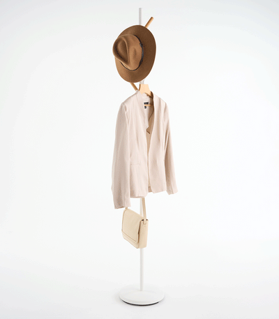 White Yamazaki Home Coat Rack (70" H) - Steel holding a brown hat near the top and a small cream shoulder bag on a lower branch, showing its tall, narrow profile.