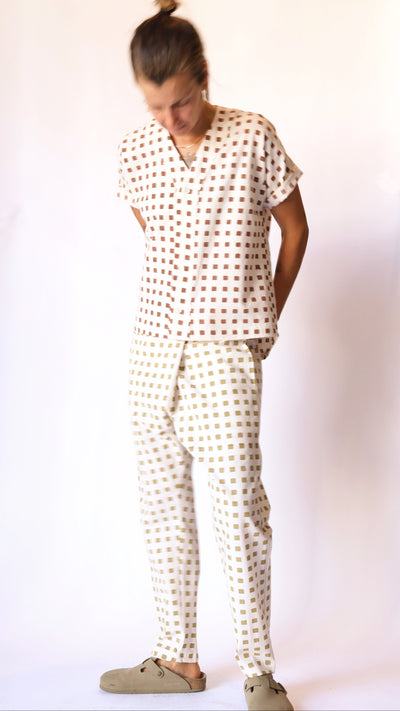 Model wearing cream Souk pants with ochre hand-block-printed squares and a matching cream shirt with rust-red squares.