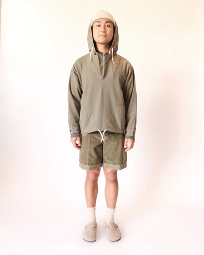 Model wearing the taupe-gray Anorak with matching shorts, a cream beanie, and slip-on shoes.
