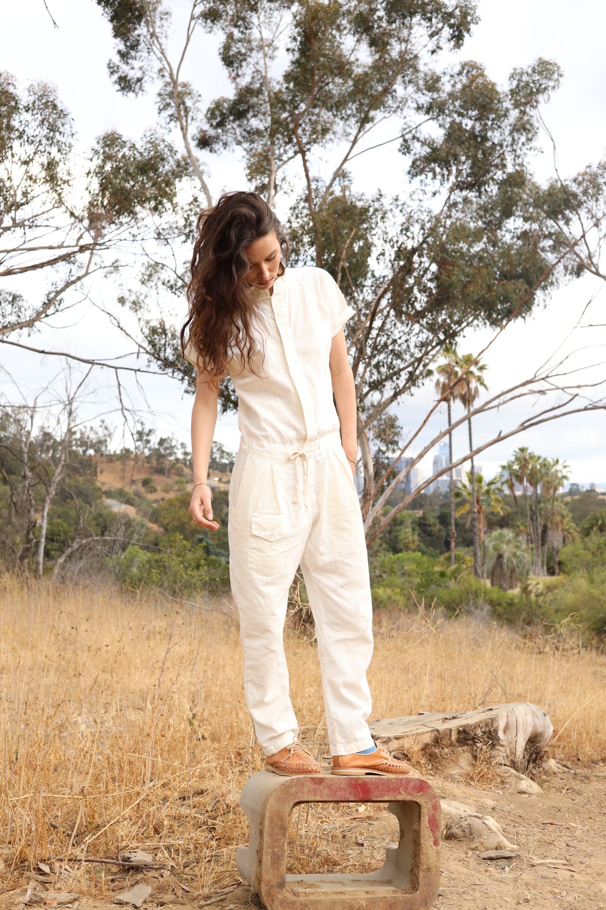 Model wearing the white short-sleeve jumpsuit in a dry grassy landscape.