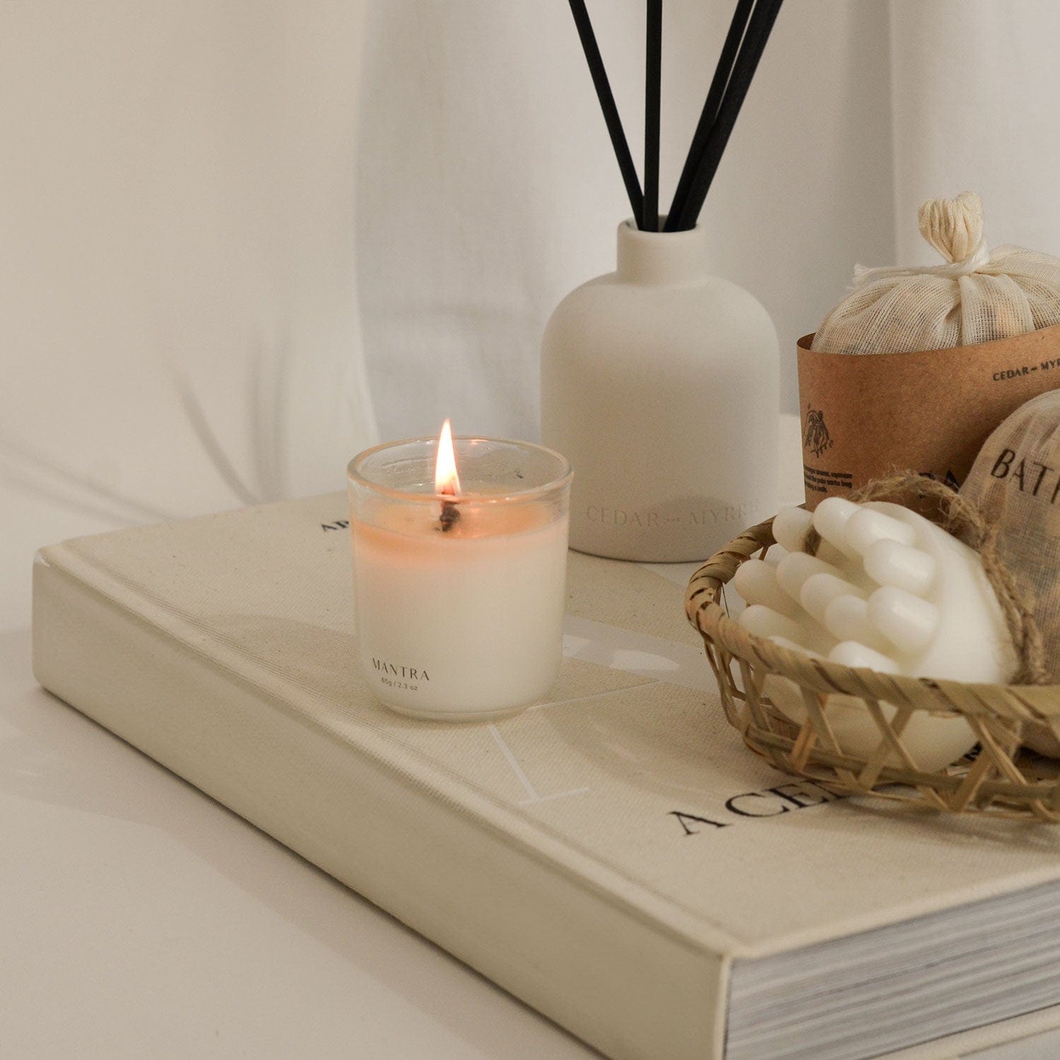 Candle burning on a book with a diffuser and basket of stones in the background