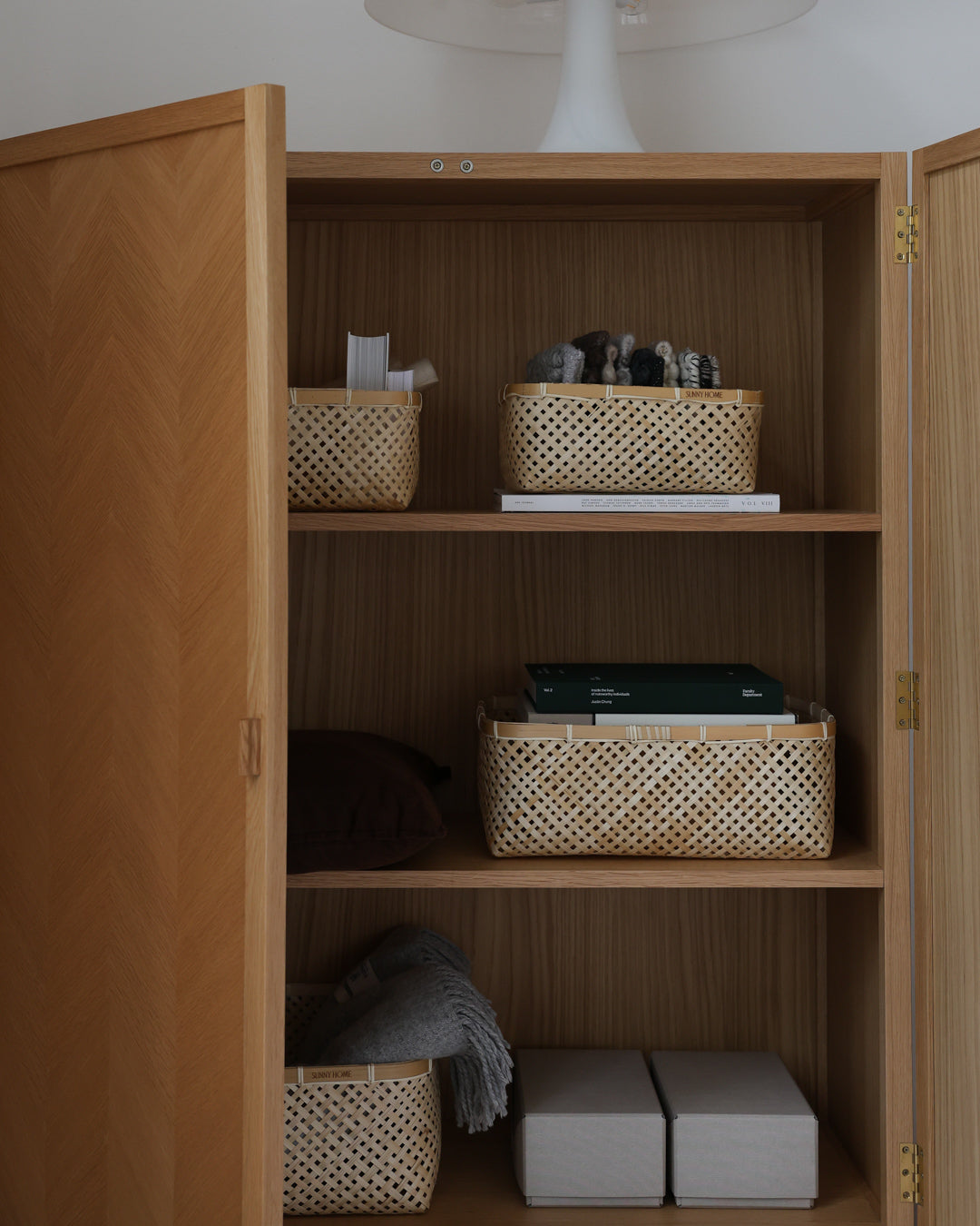 Muko baskets organizing toiletries, books, linens, and household items inside a wooden cabinet.