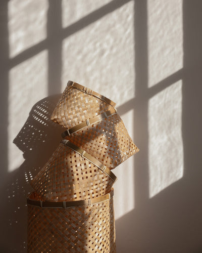 Several Muko baskets stacked at angles in warm sunlight, casting patterned shadows on the wall.