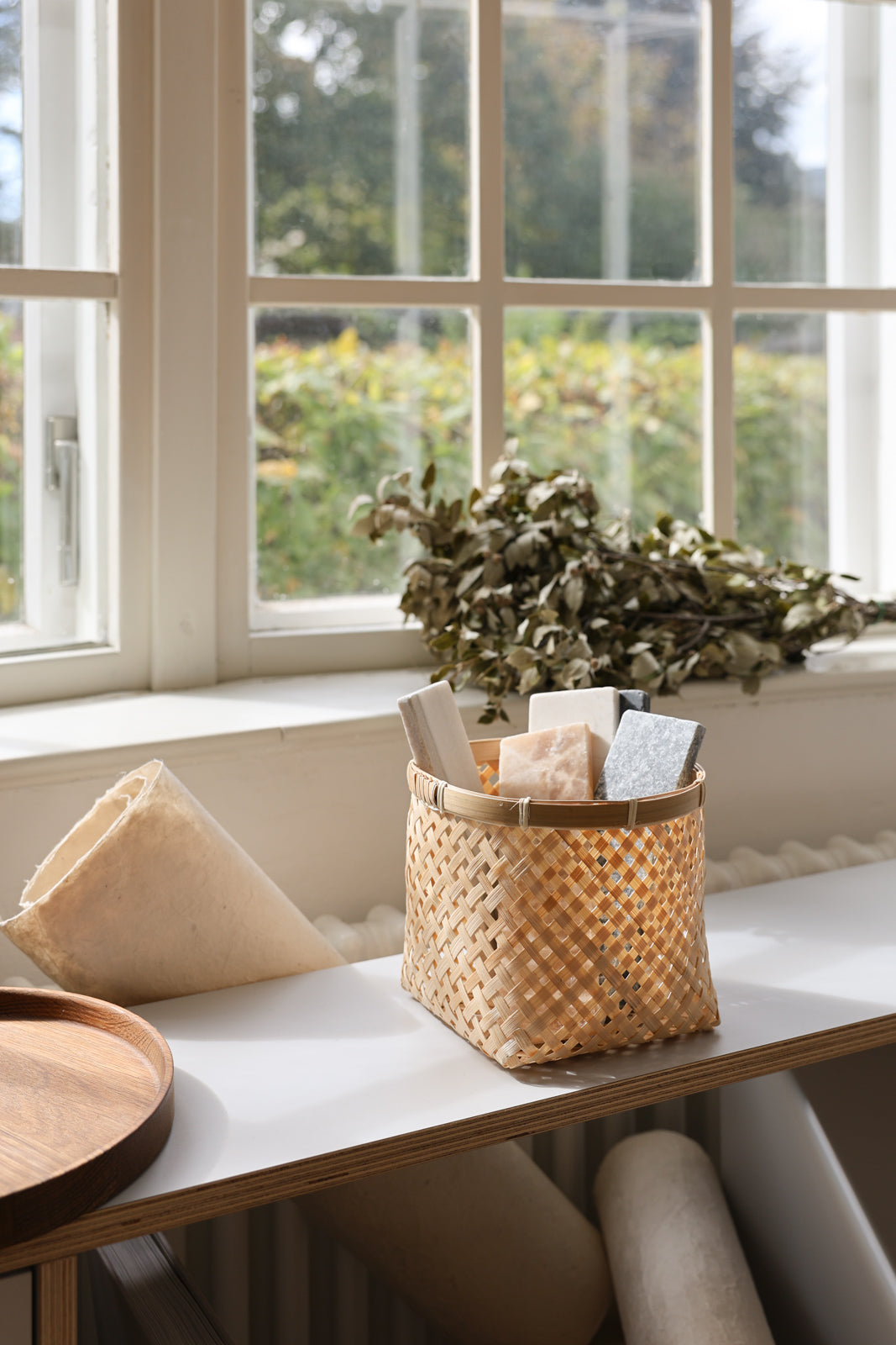 Muko basket holding papers and greenery on a table beside a bright window.