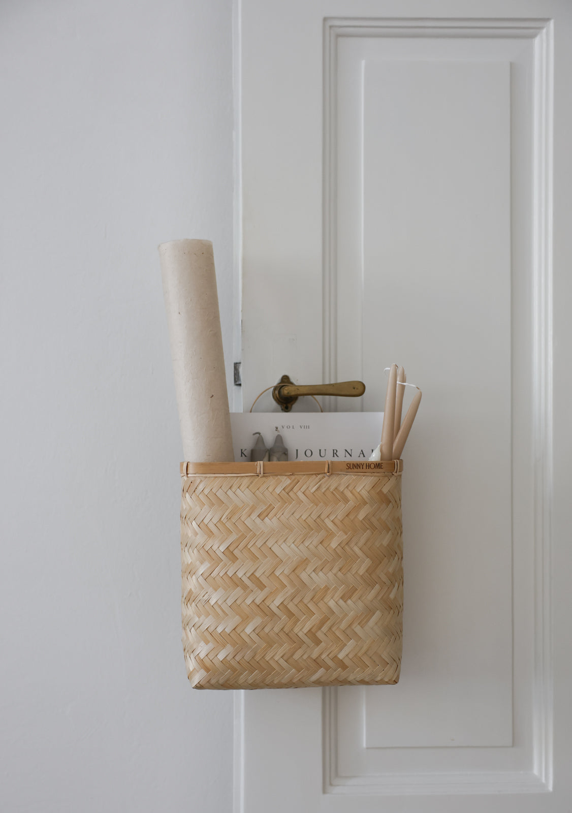 Sapa basket hanging from a paneled door and organizing rolled papers and small reading materials.