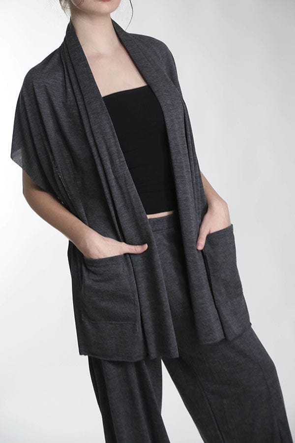 Woman wearing a charcoal merino wool pocket wrap featuring oversized pockets, soft drape, and versatile layering comfort.