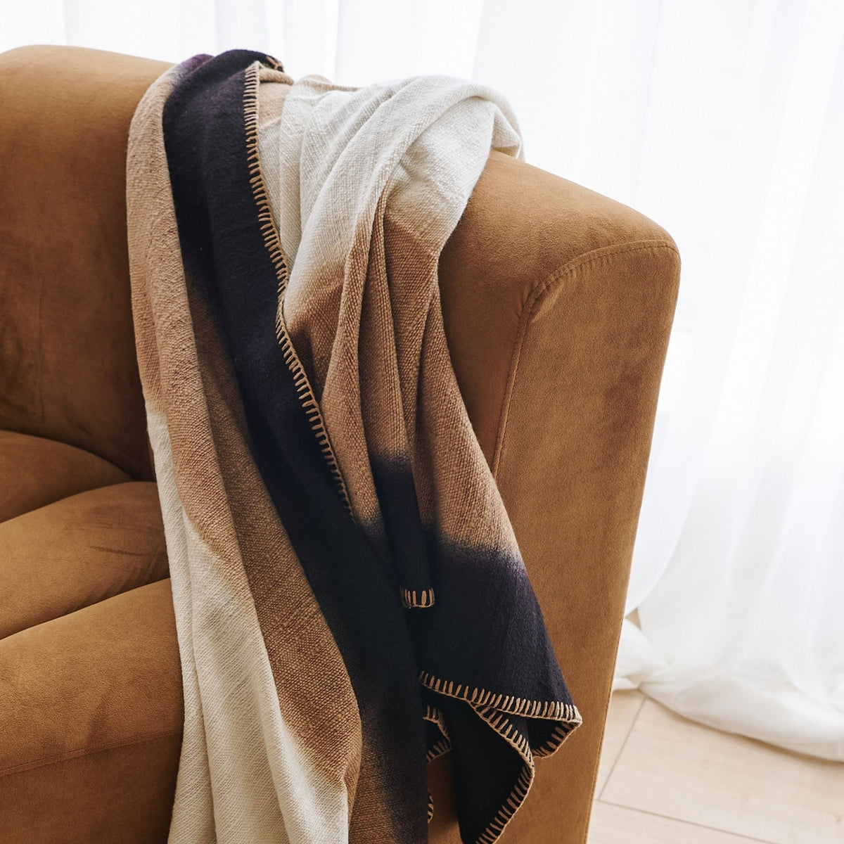 Close lifestyle view of the Siro Brown throw layered over the back and arm of a curved brown sofa