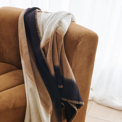 Close lifestyle view of the Siro Brown throw layered over the back and arm of a curved brown sofa