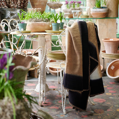 Siro Brown handwoven throw draped over a chair in a plant-filled shop, showing its tan and black panels
