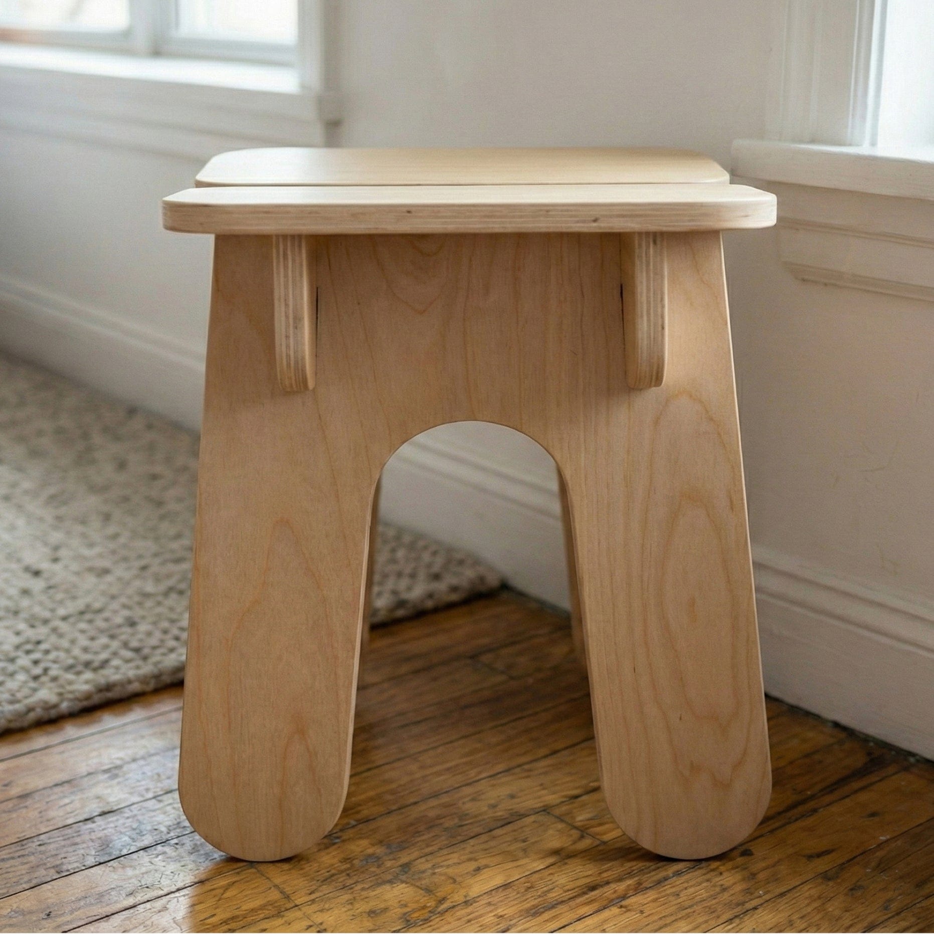 Front view of the BURIJ natural wood stool highlighting the arched opening between its wide rounded legs