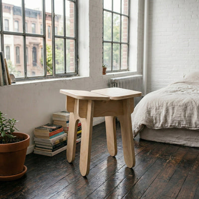 BURIJ natural wood stool beside a bedroom window with stacked books, a potted plant and an unmade bed