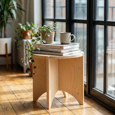 YOYO natural wood end table topped with stacked books, a small plant and a mug beside large black-framed windows