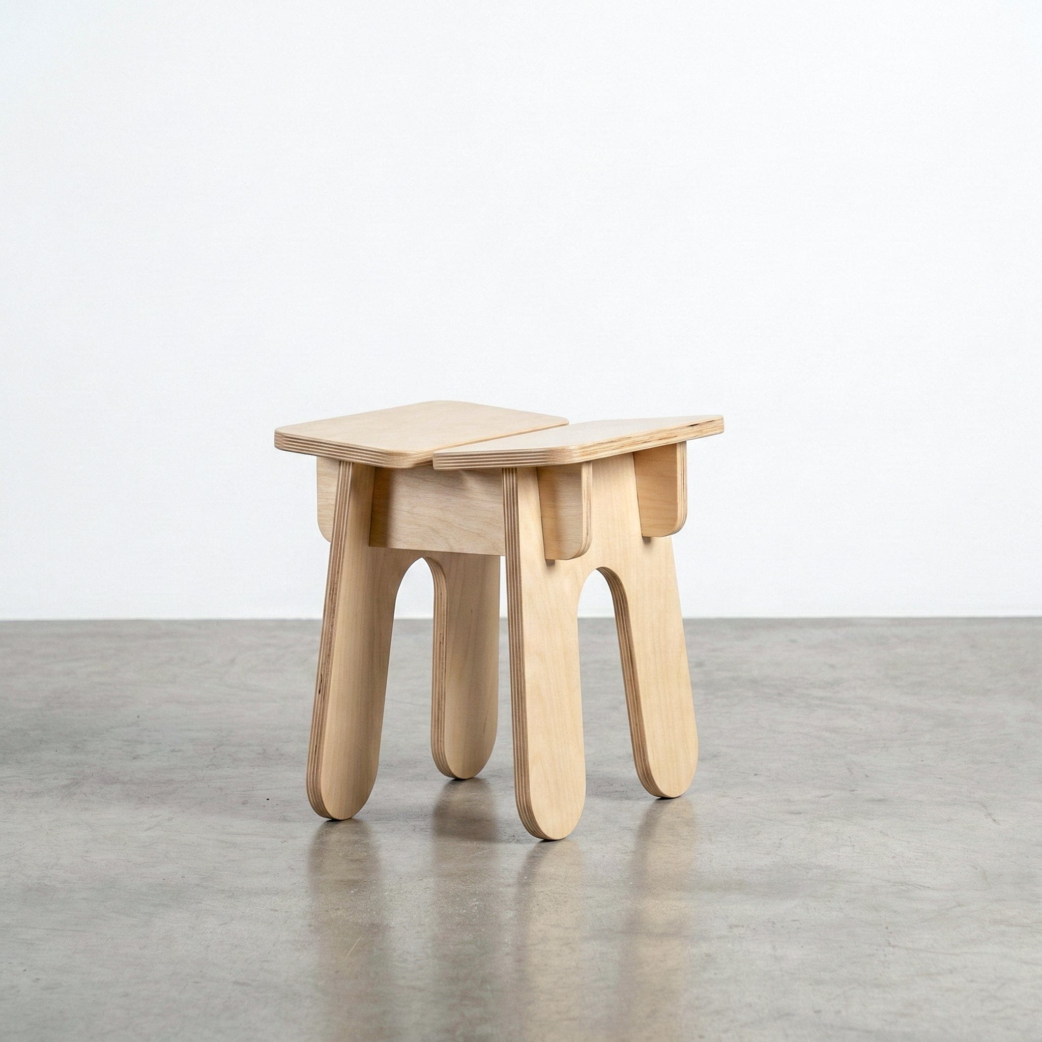 Studio Furnis BURIJ natural wood stool with a square split-panel seat, exposed joinery and four wide legs with softly rounded ends on a concrete floor