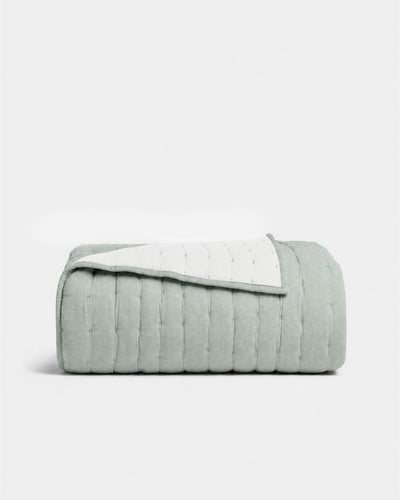 Folded sage green quilt with one corner turned back, showing its pale reverse and neatly bound edge.