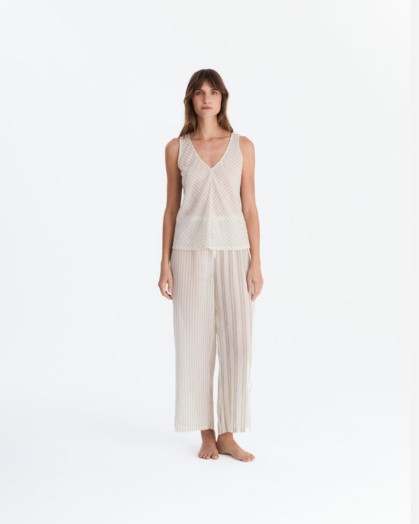 Front view of a barefoot model wearing cream and beige striped pajamas, with a sleeveless V-neck top featuring diagonal stripes and relaxed ankle-length pants with vertical stripes.