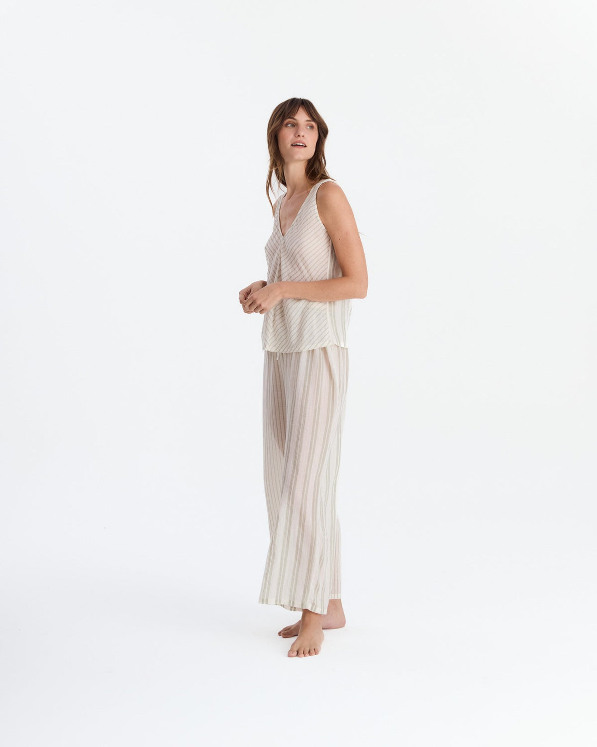Angled view of the pajama set on a barefoot model, showing the loose sleeveless top and flowing striped pants.