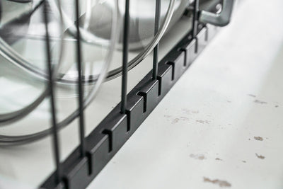 Empty black Yamazaki Home Adjustable Pot Lid Organizer - Steel shown extended, with spaced wire dividers and a caption stating it extends from 17.75 to 32.5 inches.