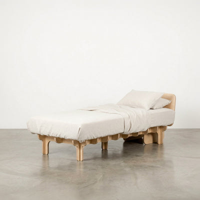 Narrow DOVID natural wood bed frame with white bedding, a low curved headboard and multiple rounded legs against a studio background