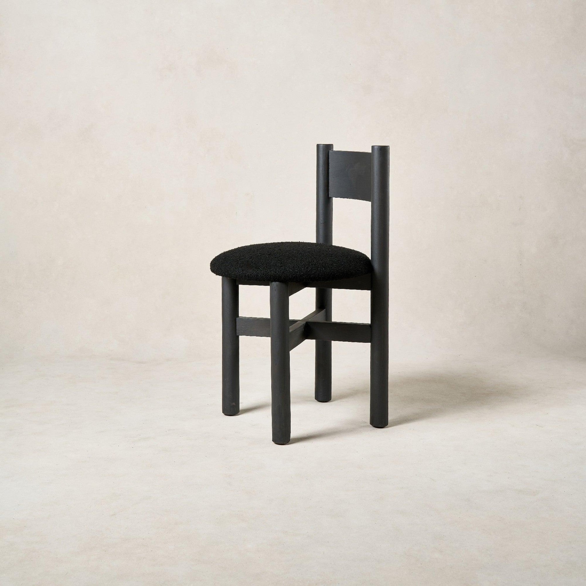 Angled view of Teddy dining chair highlighting black bouclé seat and oak frame