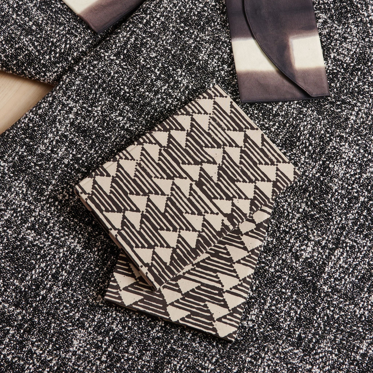 Closed Tria journal displayed on layered black-and-white textiles with its repeating geometric cover fully visible