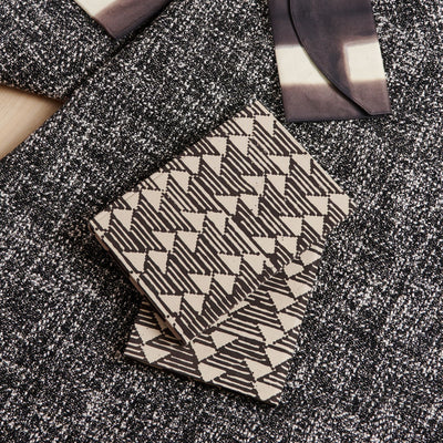 Closed Tria journal displayed on layered black-and-white textiles with its repeating geometric cover fully visible