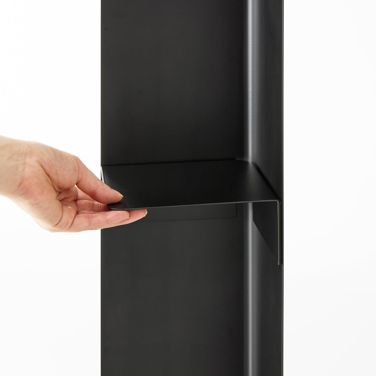 Close-up of a hand positioning the black shelf of the Yamazaki Home Rolling Bathroom Organizer - Steel against the upright panel, with its shallow raised edges visible.