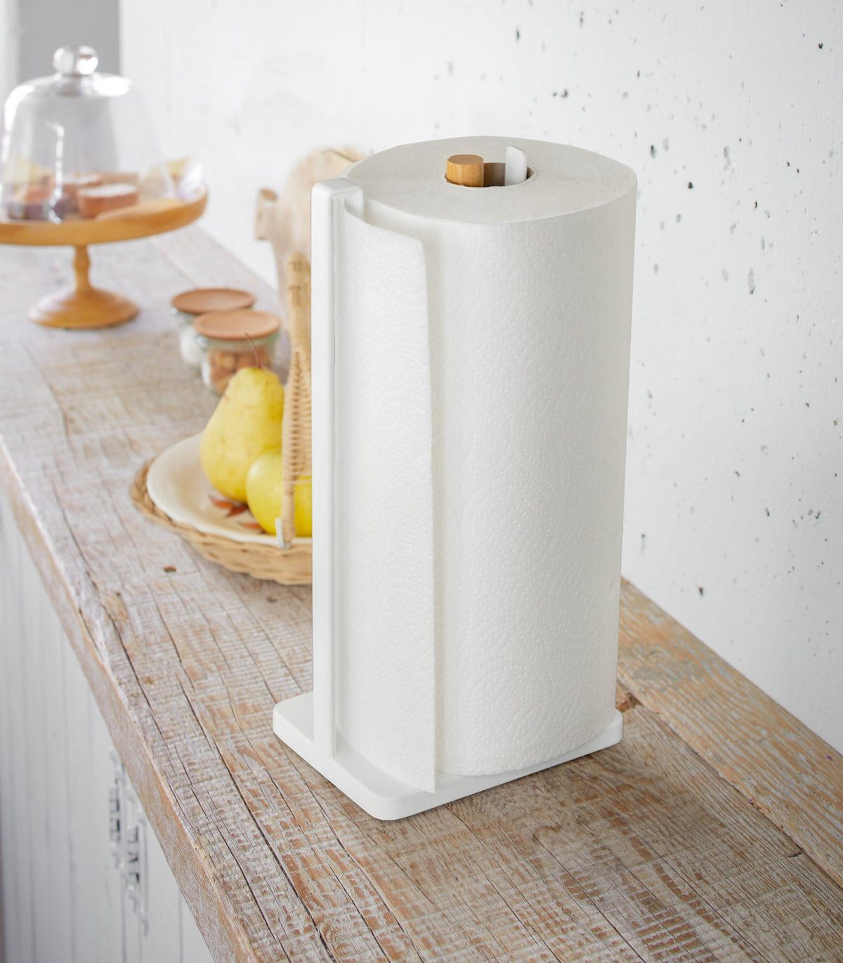 White Yamazaki Home Paper Towel Holder - Steel + Wood holding a full roll on a wooden counter, viewed from above at an angle with the wooden spindle visible at the centre.