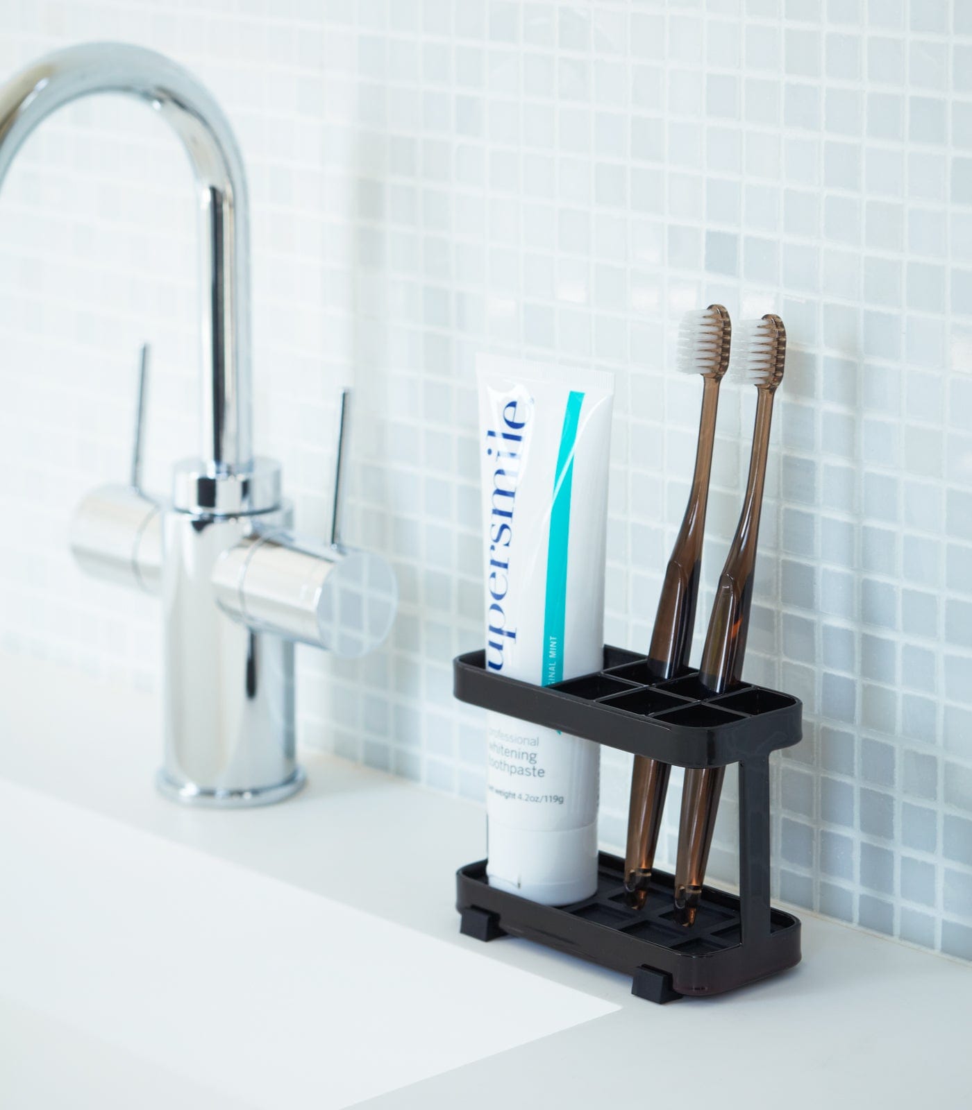 Black toothbrush holder with toothbrushes and a tube of toothpaste on a bathroom counter.