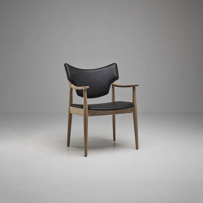 Three-quarter front view of the black Eikund Veng Arm Chair, showing the open sides, projecting wood armrests, and tapered legs against a gray studio background.