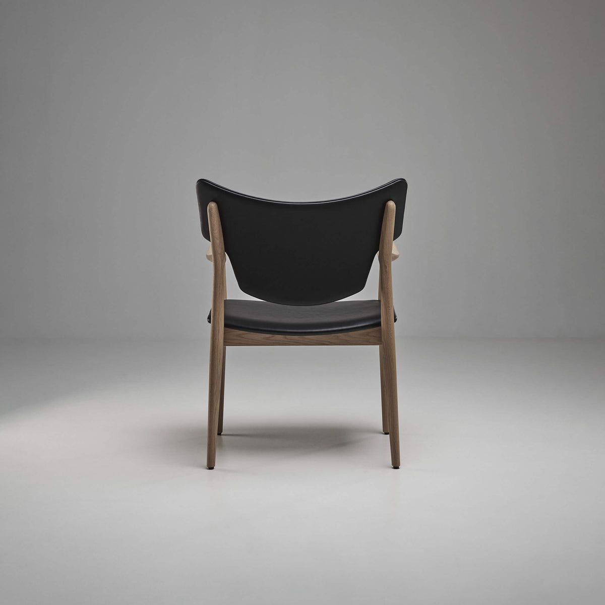 Rear view of the black Eikund Veng Arm Chair, showing the broad curved back panel, exposed wood uprights, and open lower frame.