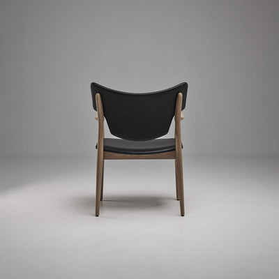 Rear view of the black Eikund Veng Arm Chair, showing the broad curved back panel, exposed wood uprights, and open lower frame.