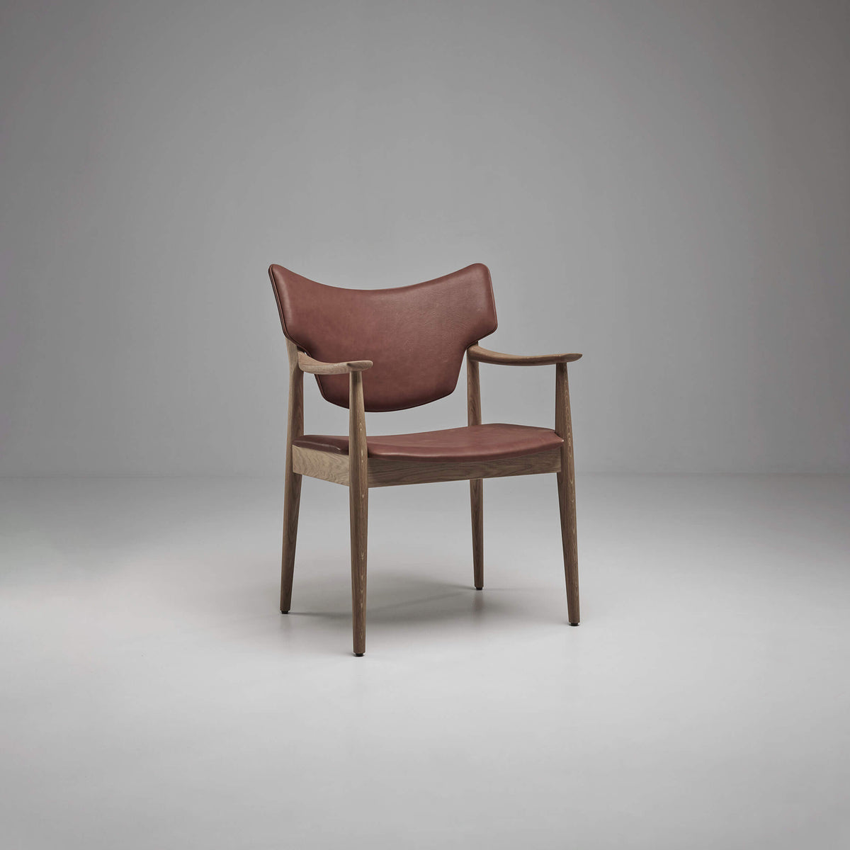 Three-quarter front view of the reddish-brown Eikund Veng Arm Chair, showing the curved back, slim wood armrests, and open space between the backrest and seat.