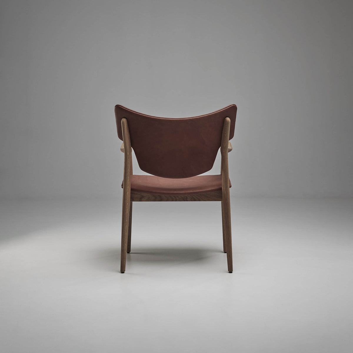 Rear view of the reddish-brown Eikund Veng Arm Chair, showing its upholstered back between dark wood supports and the matching seat below.
