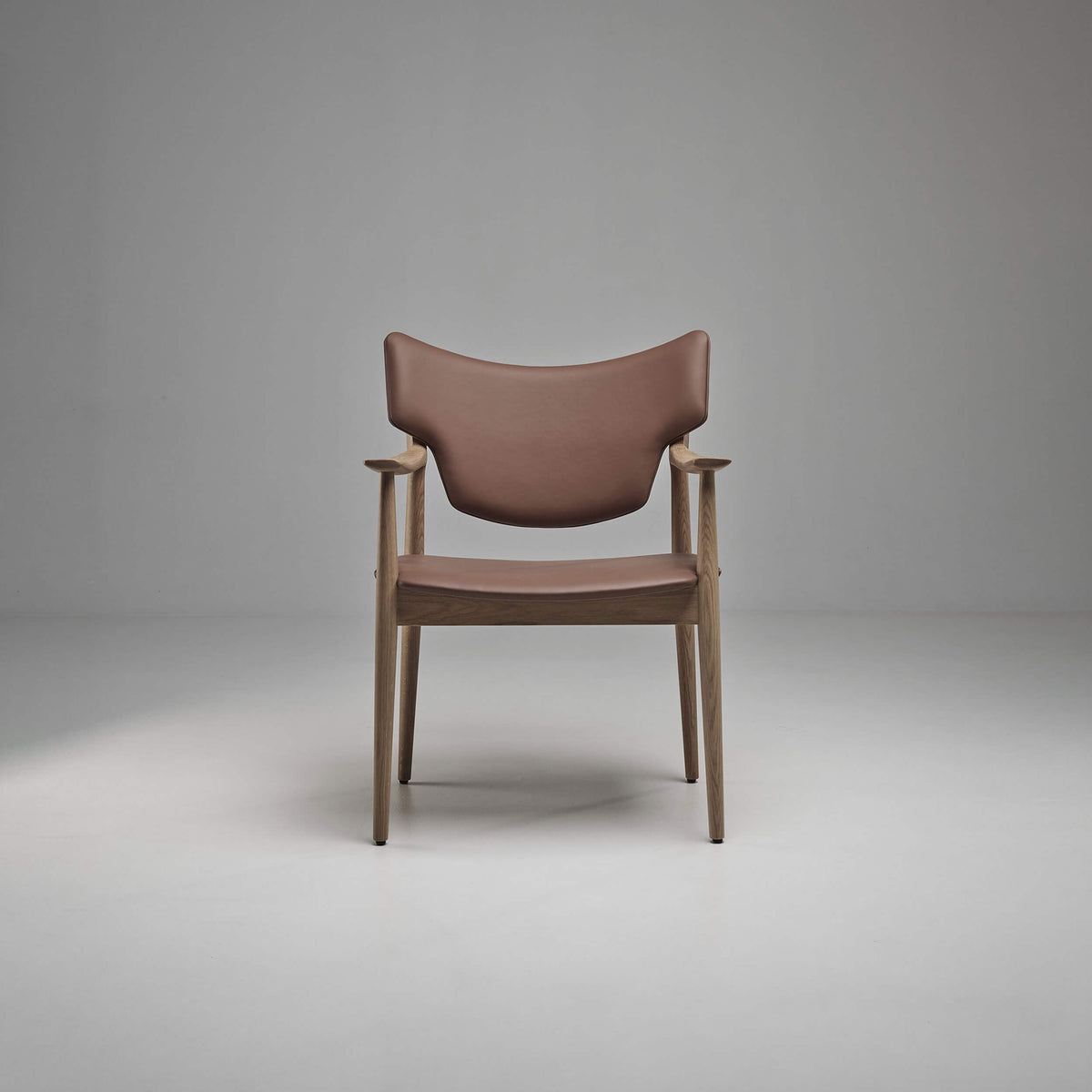 Front view of the taupe-brown Eikund Veng Arm Chair with a light brown wood frame, showing the curved backrest, narrow padded seat, and sculpted armrests.