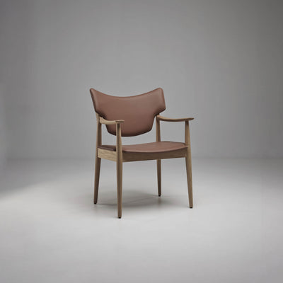 Three-quarter front view of the taupe-brown Eikund Veng Arm Chair, showing its open wood side frame, gently upturned armrest tips, and tapered legs.