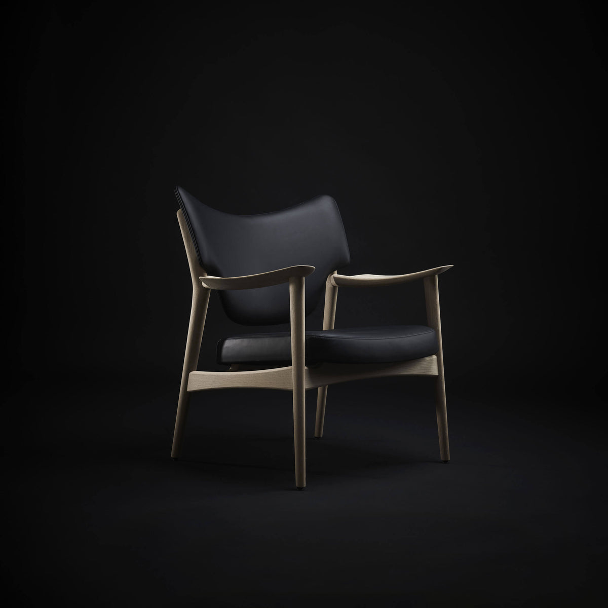 Black Eikund Veng Lounge Chair with a light wood frame in a dark studio, shown at an angle with light highlighting the curved backrest and slender arm supports.