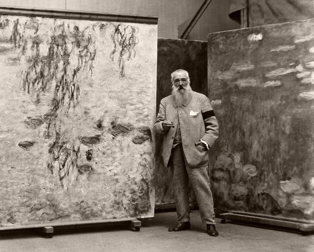 Black-and-white archival photograph of an artist standing beside large abstract canvases.