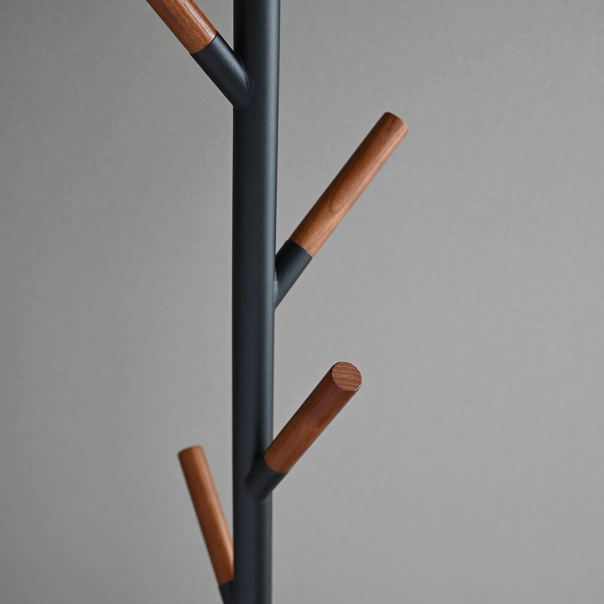 Detail of the black Yamazaki Home Coat Rack (70" H) - Steel branches, showing upward-angled supports capped with cylindrical brown wood tips.