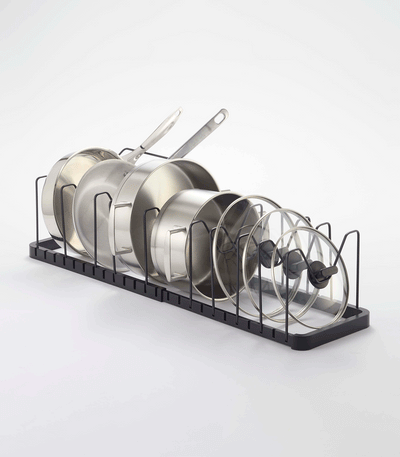 Black Yamazaki Home Adjustable Pot Lid Organizer - Steel fitted lengthwise inside an open kitchen drawer, with pans and lids arranged beside storage canisters.