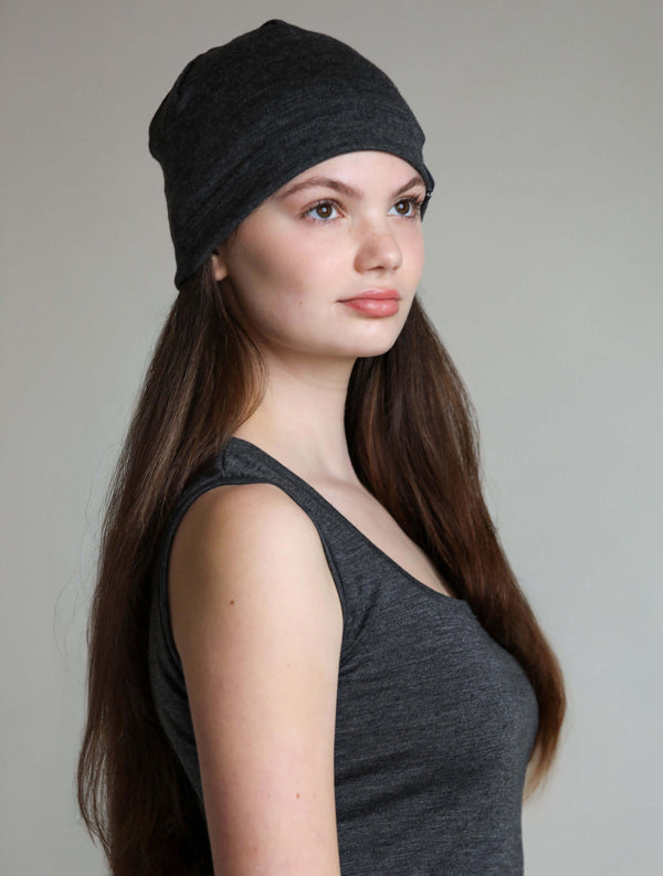 Woman wearing a charcoal merino wool sauna beanie designed to protect hair and scalp during sauna and wellness rituals.