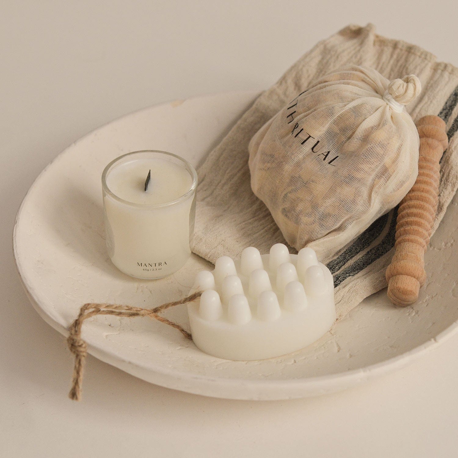 White ceramic dish with a candle, scrubber, and other items on a neutral background