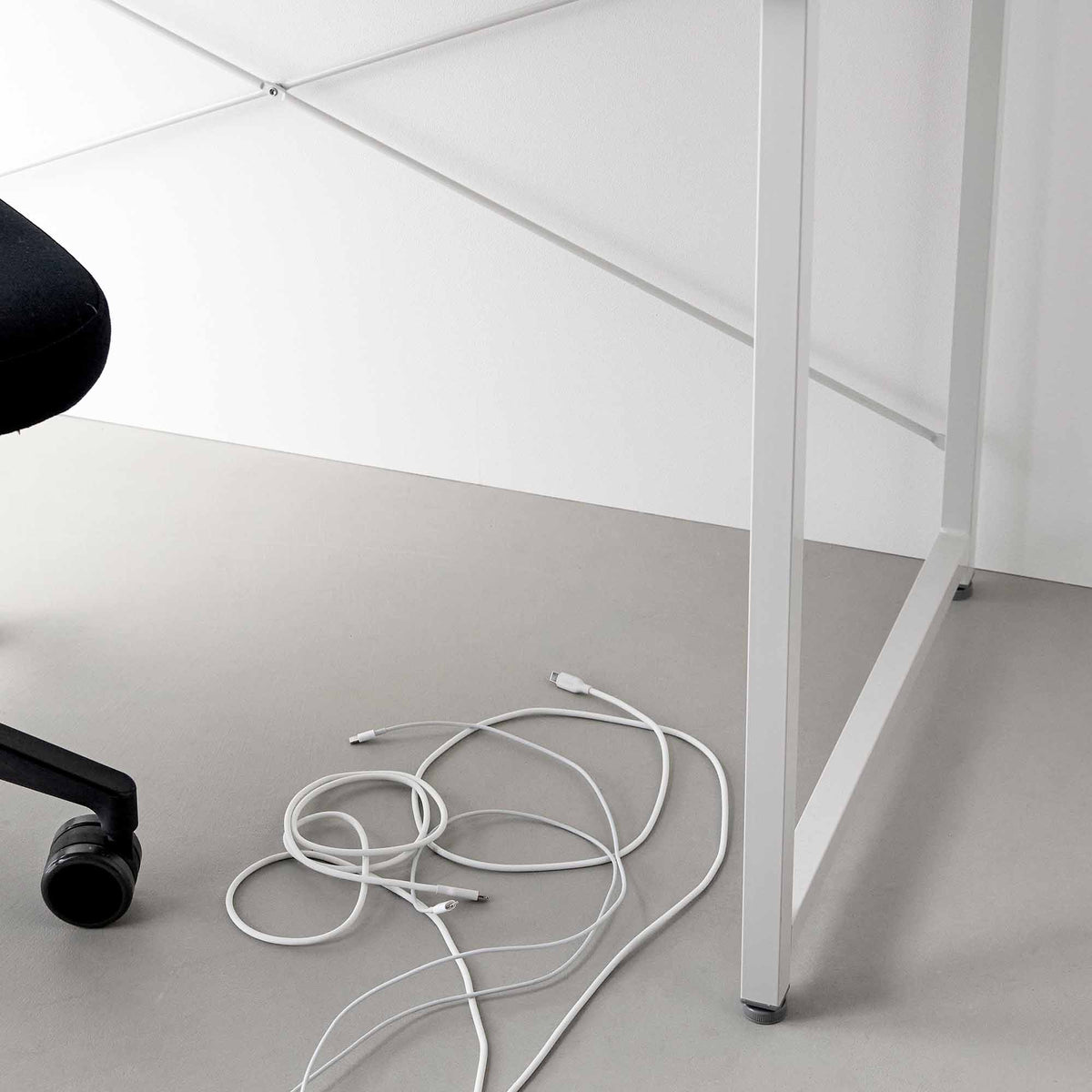 White cables lie loosely tangled on the grey floor beneath a white desk, showing the floor area used in the Yamazaki Home Magnetic Cable Holders With Adhesive Steel Bases (Set of 5) - Silicone demonstration.