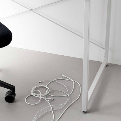 White cables lie loosely tangled on the grey floor beneath a white desk, showing the floor area used in the Yamazaki Home Magnetic Cable Holders With Adhesive Steel Bases (Set of 5) - Silicone demonstration.
