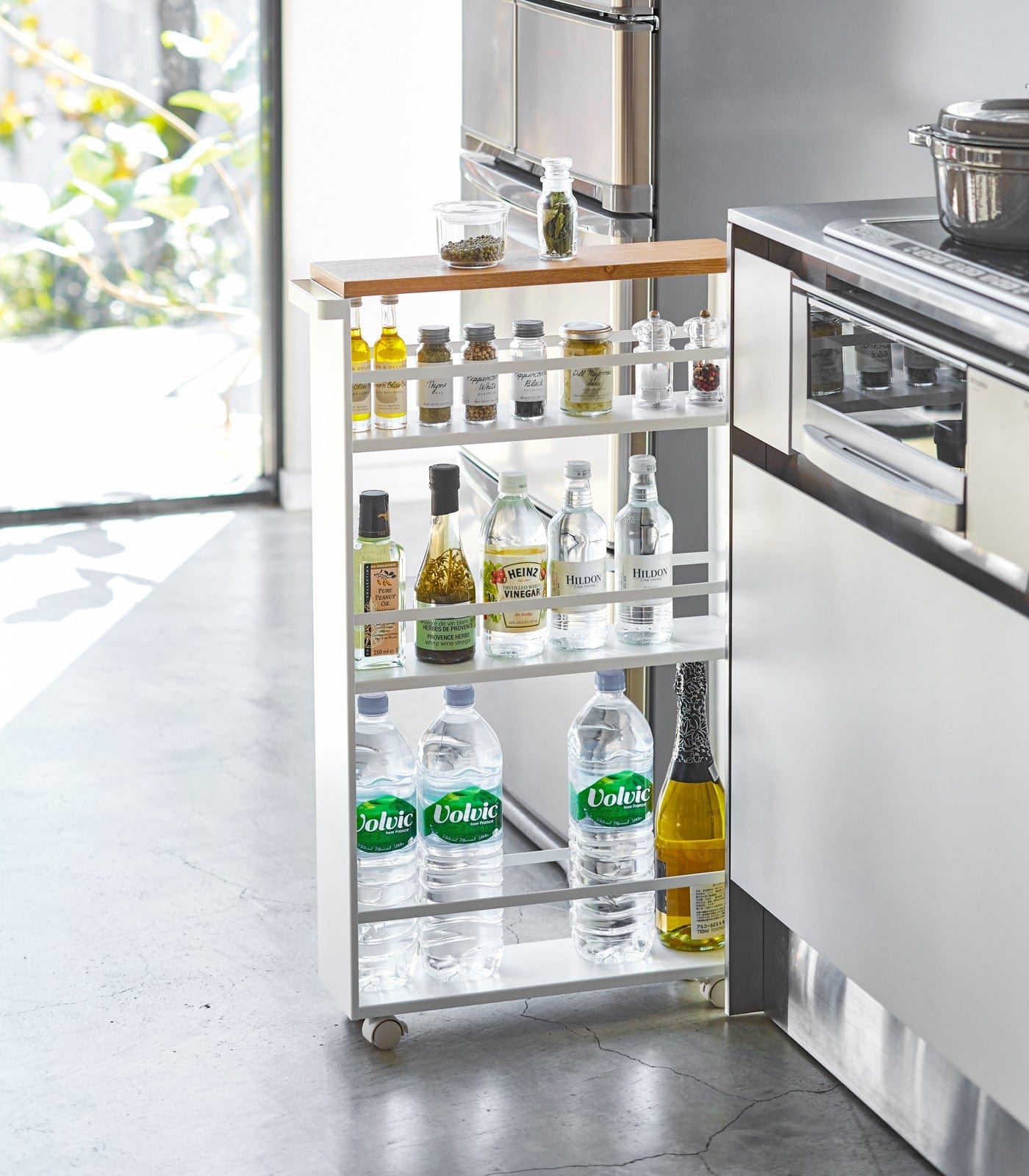 Kitchen island cart with various bottles in a modern kitchen setting. Slim Storage Cart (32&quot; H)  - Steel