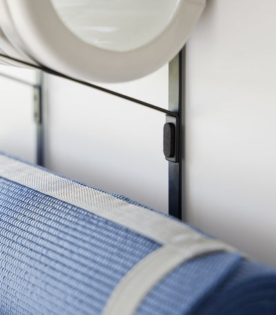 Detail of the black Yamazaki Home Over-the-Door Fitness Equipment Hanger - Steel rail and support attachment, showing the dark connection beside the blue mat and below the grey roller.