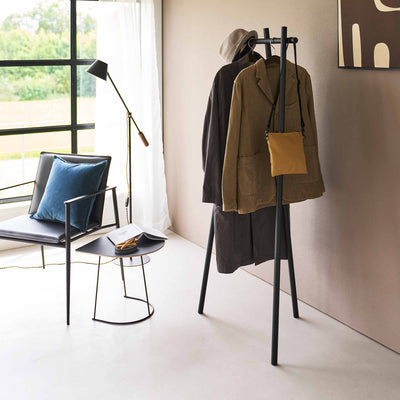 Black Yamazaki Home Tri-Post Coat Rack (60" H) - Steel styled with layered dark and olive-brown coats, a hat and mustard shoulder bag, showing several items arranged across the upper rail.