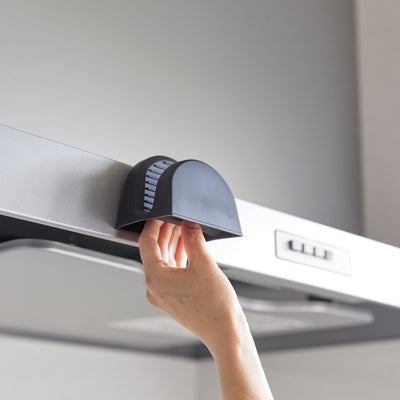 Close-up of a hand reaching into a black Yamazaki Home Magnetic Pot Holder - Silicone stored on the front edge of a range hood.