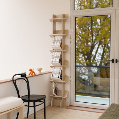 Yankel tall bookcase displaying magazines beside a glass door, dining chair and round table in a bright room