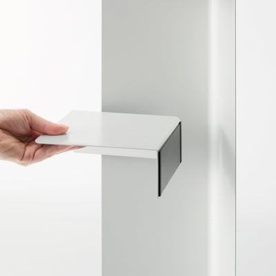 Close-up of a hand holding the white shelf component of the Yamazaki Home Rolling Bathroom Organizer - Steel away from its vertical panel, showing the flat surface and downward-bent side.