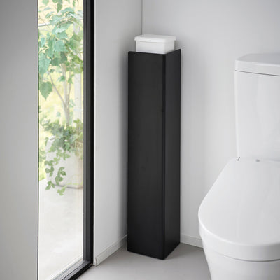 Black Yamazaki Home Rolling Bathroom Organizer - Steel with its tall solid panel facing outward beside a toilet, concealing the shelves while a white tissue box rests on top.